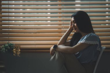 Üzgün ve bunalımlı genç bir kadın oturma odasının penceresinde oturuyor, üzgün bir ifadeyle dışarı bakıyor, bitkinlik, yalnızlık ve mutsuzluğu iletiyor.