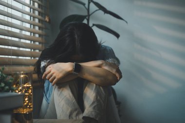 Üzgün ve bunalımlı genç bir kadın oturma odasının penceresinde oturuyor, üzgün bir ifadeyle dışarı bakıyor, bitkinlik, yalnızlık ve mutsuzluğu iletiyor.