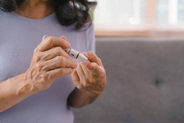 Close-up of a senior woman's hand checking her blood sugar level with a glucometer by herself at her home