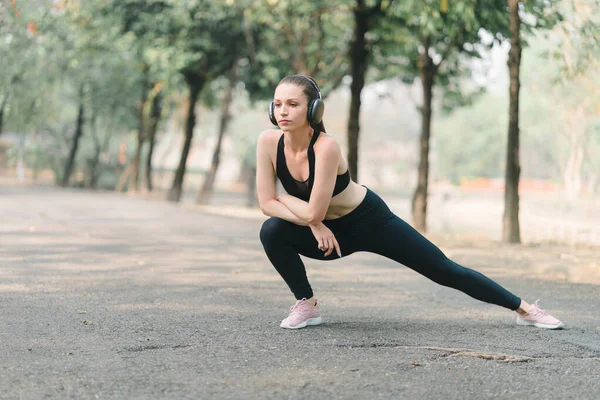 stock image A young female athlete, dressed for running, is shown stretching her legs in preparation for a jog through the park