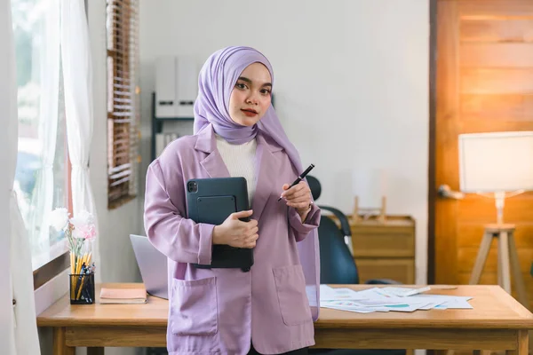 一个美丽的穆斯林千年亚洲女商人头戴紫色头巾在自家办公室远程办公的肖像 看着相机 — 图库照片