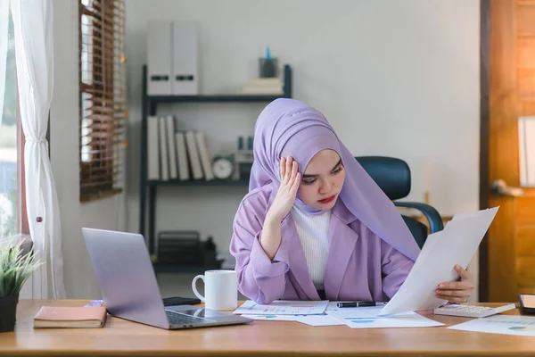 stock image A young Muslim businesswoman wearing a purple hijab is working from home and appears stressed while using her laptop, looking worn out and anxious