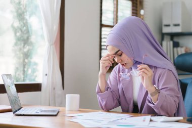 Stresli Müslüman milenyum iş kadını evde çalışan mor bir başörtüsü takıyor endişeli, yorgun ve bunalmış görünüyor.