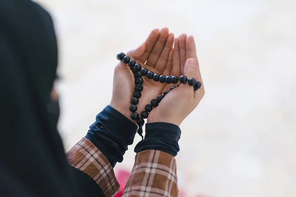 A close-up shot hands of a Muslim woman holding a rosary while wearing a long hijab, as she prays and makes dua to Allah, the Muslim God, at the mosque during an Islamic religious ceremony