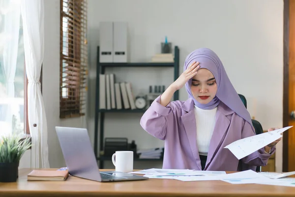 Stock image Stressed Muslim millennial businesswoman wearing a purple hijab working from home on laptop looking worried, tired and overwhelmed