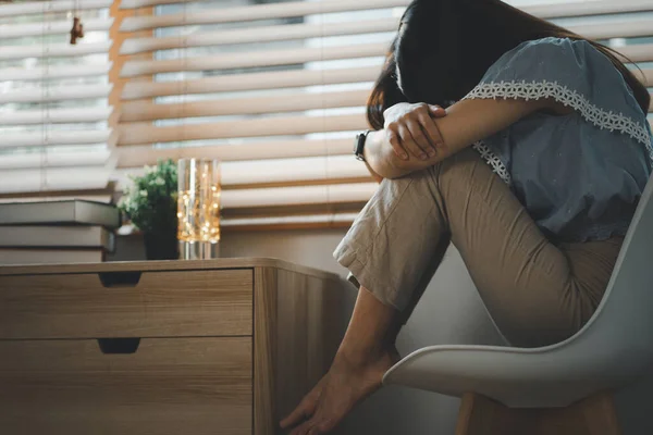 stock image Sad and depressed young woman sitting nere window in the living room, looking outside with a sad expression, conveying feelings of exhaustion, loneliness, and unhappiness. Vintage style.