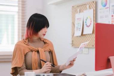 Yaratıcı ve stil sahibi genç bir kadın serbest tasarımcı ofisinde masasında otururken bir tablet ve stil kalem kullanıyor.