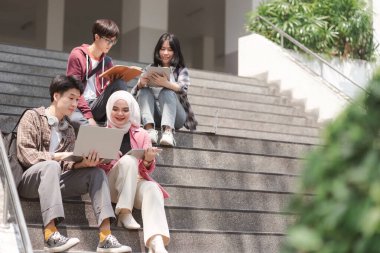 Üniversite öğrencilerinden oluşan çok ırklı bir grup, kampüsün yakınındaki basamaklarda oturup birbirleriyle iletişim kurarken birlikte öğrenim görüyor.