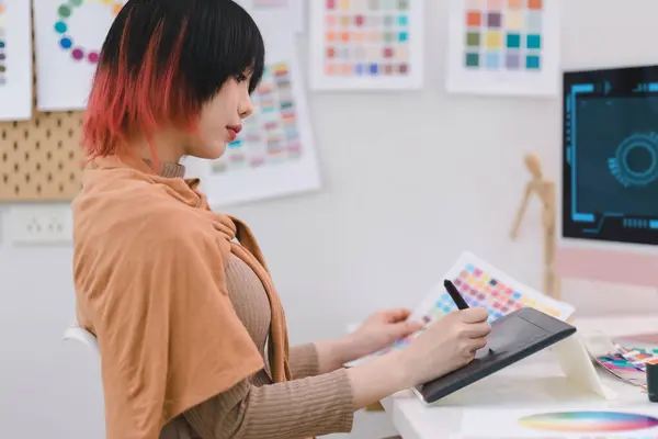 stock image Young graphic designer using a tablet and stylus pen while sitting at her desk in office