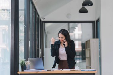 Bir iş kadını mutlu ve başarılı bir pozda dizüstü bilgisayara bakarken kollarını kaldırarak kutlama yapar.