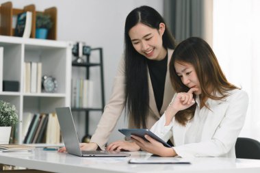 İki profesyonel Asyalı girişimci iş adamı bir konferans odasında değerlendirme verilerini tartışıyor, büyümeye odaklanıyor ve bir mali hesap grafiğine işaret ediyorlar,