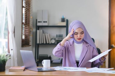 Stresli Müslüman milenyum iş kadını evde çalışan mor bir başörtüsü takıyor endişeli, yorgun ve bunalmış görünüyor.