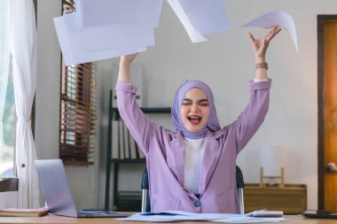 Asabi Müslüman milenyum iş kadını ofis masasında oturan tesettüre oturmuş hayal kırıklığına uğramış yüz ifadesi olan kağıtları kusuyor. Negatif insan duyguları