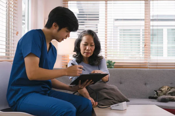 Young Asian male nurse, assisted living in-home carer, or doctor visiting an old senior citizen at home to talk about result follow-up checklist, healthcare advice, or prescription