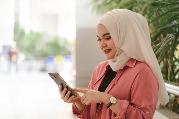 一名身穿白头巾的穆斯林大学生坐在校园里 手持并使用智能手机 — 图库照片
