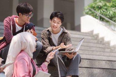 Üniversite öğrencilerinden oluşan çok ırklı bir grup, kampüsün yakınındaki basamaklarda oturup birbirleriyle iletişim kurarken birlikte öğrenim görüyor.