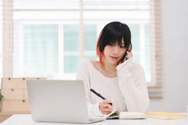 stock image A young Asian female is using her laptop to communicate over the internet from her cozy home office workplace. This depicts the concept of remote work and e-learning