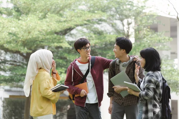 多様性に富んだ多人種の若いアジアの大学生のグループは 授業の合間にキャンパス内で休んでおしゃべりしているのを見ています 彼らは笑顔で 自分自身を楽しんでいるようです — ストック写真