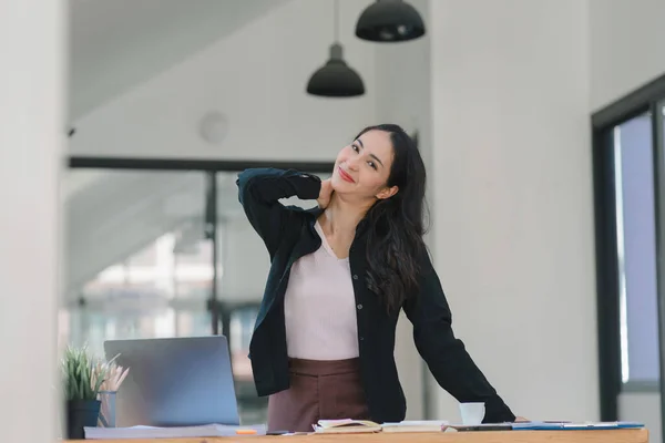 An attractive young Asian millennial businesswoman is stretching her arms during a break in the office