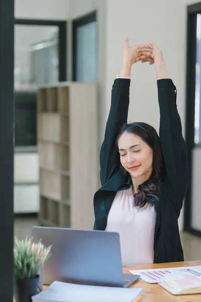 An attractive young Asian millennial businesswoman is stretching her arms during a break in the office