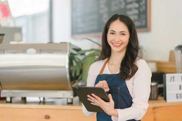 stock image Portrait of confident female barista standing at counter. Woman cafe owner in apron looking at camera and smiling while welcoming guests