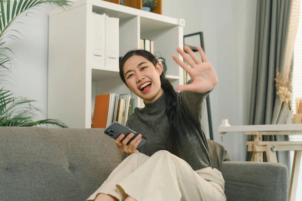 Stock image Charming Asian woman is using her smartphone while relaxing on the sofa at home