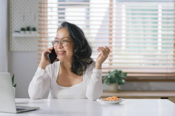 The Senior businesswoman adviser is analyzing and discussing the financial report situation on smartphone in her home office, financial, accounting, and investment advisor concepts