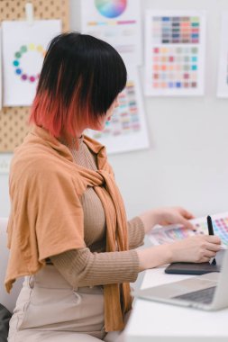 Yaratıcı genç grafik tasarımcısı örnekleyiciden bir renk seçiyor ve iş yerindeki dijital tablet bilgisayarda çiziyor
