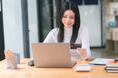 Dizüstü bilgisayar ve el ele tutuşan bir kadının iş yerinde çekilmiş beyaz kredi kartı maketi..