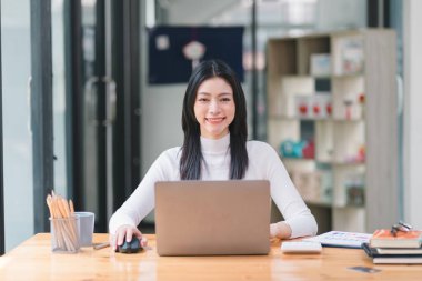 Başarılı ve güzel bir Asyalı iş kadını, sekreter, satış müdürü ya da iş danışmanı portresi, iş yerinde dizüstü bilgisayarla oturuyor, gülümsüyor ve günlük kıyafetlerini giyiyor.