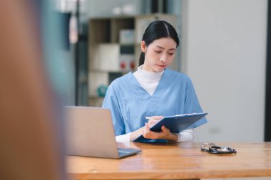 Kendine güvenen, güzel, profesyonel, bin yıllık bir kadın doktor ya da hemşire bir hastane danışma odasında bir masada otururken bilgisayarla çalışıyor.