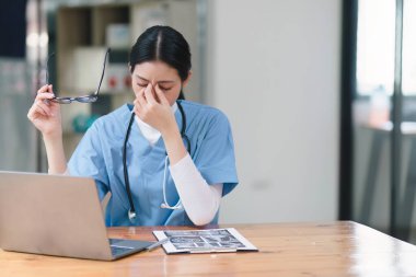 Profesyonel milenyum kadın doktoru ya da hemşire bir masada otururken dizüstü bilgisayar ve dosya üzerinde gergin bir ifadeyle çalışıyor.