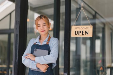 Tezgahta duran kendinden emin kadın baristanın portresi. Önlüklü kadın kafe sahibi kameraya bakıyor ve misafirleri ağırlarken gülümsüyor.