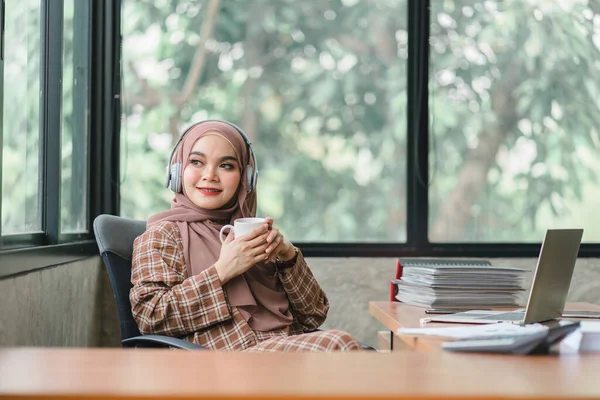 茶色のヒジャーブを身に着けている自信に満ちた 美しく プロの 千年のイスラム教徒のアジアのビジネス女性は彼女のオフィスでリラックスしてコーヒーを飲んでいます — ストック写真