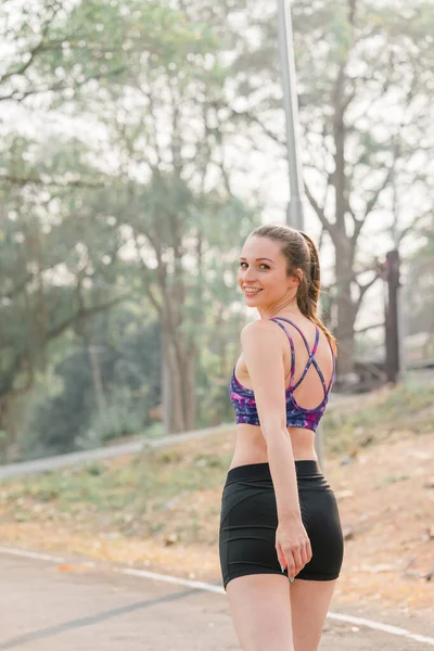 A beautiful sportswoman in sportswear is jogging outdoors in Autumn city park background