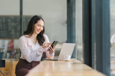 Kafedeki güzel Asyalı iş kadını, akıllı telefon kullanıyor ve gülümsüyor.