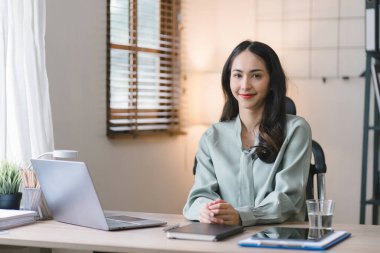 Genç, neşeli, mutlu, pozitif, sevimli ve güzel bir Asyalı iş kadınının portresi. Bir ev ofisinde otururken finans ve pazarlama projeleri üzerinde çalışıyor.