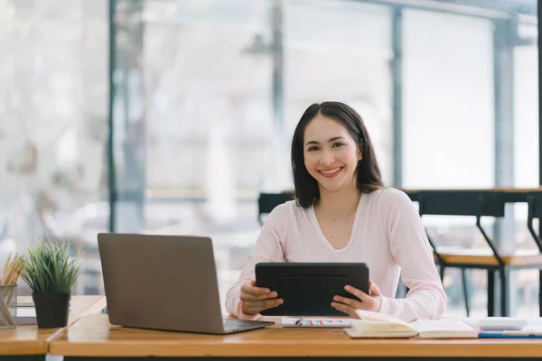 stock image A portrait of a smiling, young, beautiful, professional, and confident millennial Asian businesswoman using a digital tablet to analyze sales data at a co-working space