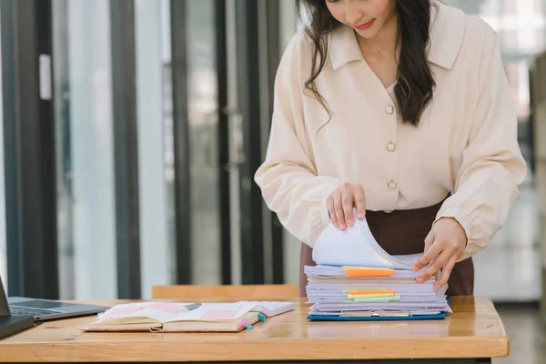 stock image Businesswoman's hands are busy searching and checking stacks of paper files for unfinished documents, with folders and papers piled up on her busy work desk in the office