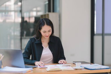 Gülümseyen, genç, güzel, profesyonel ve kendine güvenen Asyalı bir iş kadınının dijital tableti kullanarak ortak çalışma alanındaki satış verilerini analiz eden bir portresi.