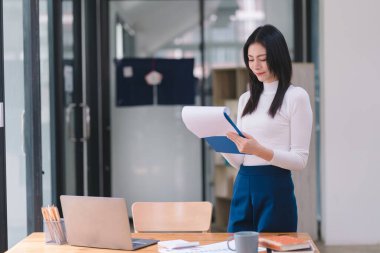 Başarılı ve güzel bir Asyalı iş kadını, sekreter, satış müdürü ya da iş danışmanı portresi, iş yerinde dizüstü bilgisayarla oturuyor, gülümsüyor ve günlük kıyafetlerini giyiyor.