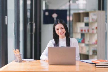 Gülümseyen, genç, güzel, profesyonel ve kendine güvenen Asyalı bir iş kadınının dijital tableti kullanarak ortak çalışma alanındaki satış verilerini analiz eden bir portresi.