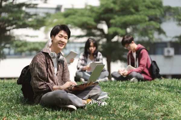 キャンパスの近くの芝生の上に座りながら アジアの大学生の多民族グループが一緒に勉強しているのが見えます — ストック写真