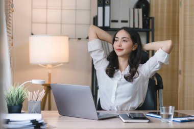 Stresli ve yorgun milenyum iş kadını ofis masasında eli başının üstünde otururken görülüyor. Bu da yoğun bir iş günü geçirdiğini gösteriyor.