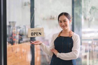 Tezgahta duran kendinden emin kadın baristanın portresi. Önlüklü kadın kafe sahibi kameraya bakıyor ve misafirleri ağırlarken gülümsüyor.