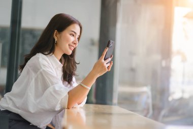 Beautiful young millennial Asian woman using a smartphone at a cafe. Portrait of a gorgeous smiling female engrossed in her mobile phone