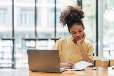 Genç Afrikalı Amerikalı bir kadın web sitesi kursunu izlerken not alıyor. Afro-Amerikalı öğrenci e-öğrenme yoluyla online çalışmak için konferansı dinliyor