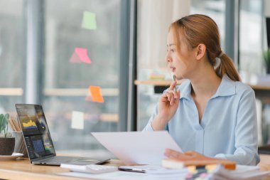 İş kadını muhasebeci yeni satış stratejileri planlamak için piyasa verilerini, bilançolarını, hesaplarını ve net kârlarını analiz etmek için bir hesap makinesi, grafikler ve grafikler kullanıyor.