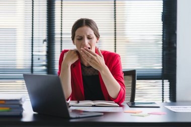Stresli ve yorgun milenyum iş kadını ofis masasında eli başının üstünde otururken görülüyor. Bu da yoğun bir iş günü geçirdiğini gösteriyor.