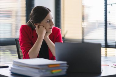 Stresli ve yorgun milenyum iş kadını ofis masasında eli başının üstünde otururken görülüyor. Bu da yoğun bir iş günü geçirdiğini gösteriyor.